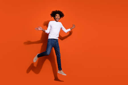 Photo of pretty impressed guy dressed white shirt running fast jumping high empty space isolated orange color backgroundの写真素材