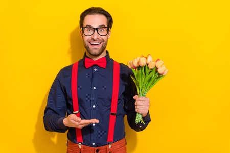 Photo of young excited handsome man present tulips plant recommend promoter isolated over yellow color backgroundの写真素材