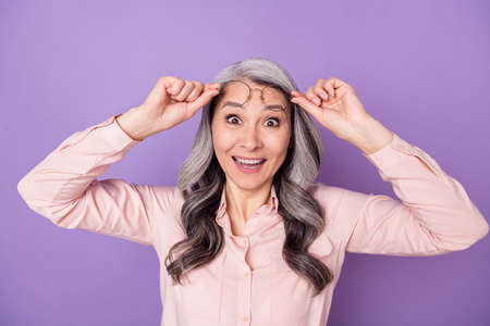 Portrait of attractive cheerful amazed funny glad woman touching eyewear great news reaction isolated over violet purple color backgroundの写真素材