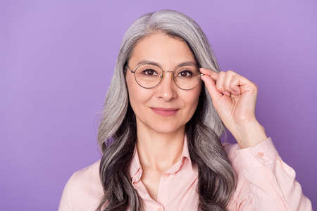 Portrait of attractive trendy intellectual cheery woman touching eyewear isolated over violet purple...