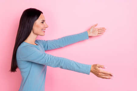 Photo of funny adorable woman wear blue shirt holding arms empty space smiling isolated pink color...