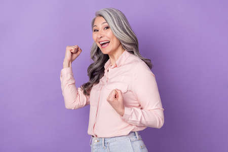 Portrait of attractive cheerful lucky grey-haired woman rejoicing having fun isolated over violet...