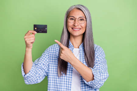 Photo of impressed elder white hairdo lady index card wear eyewear plaid shirt isolated on green color backgroundの写真素材