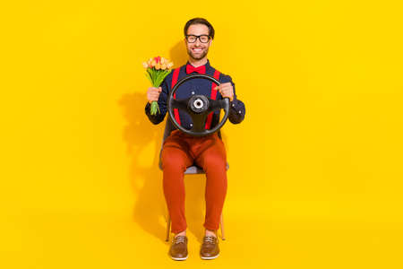 Full length photo of young guy ride automobile vehicle road hold tulips present isolated over yellow color backgroundの写真素材