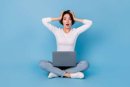 Photo of shiny impressed woman wear white shirt legs crossed reading modern gadget isolated blue...