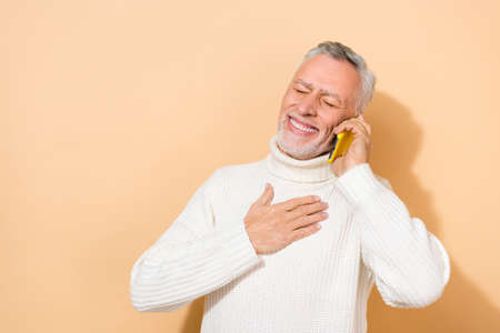 Portrait of attractive dreamy cheerful grey-haired man calling friend roaming service isolated over beige pastel color backgroundの写真素材