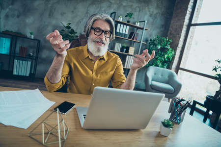Photo of cheerful mature guy dressed yellow shirt spectacles video talk modern gadget indoors workplace workstationの写真素材