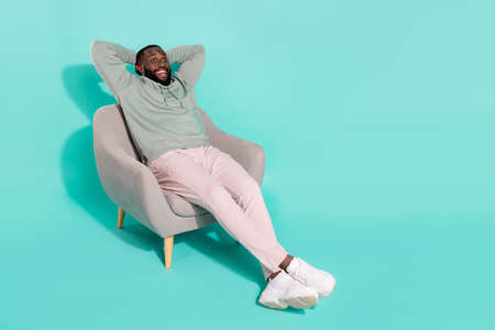 Full length body size view of attractive cheery glad amazed guy sitting in cosy armchair isolated over shine teal turquoise color backgroundの写真素材