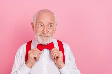 Portrait of attractive cheerful gray-haired guy wearing fixing bowtie festal occasion isolated over pink pastel color backgroundの写真素材