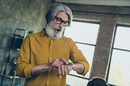 Portrait of attractive worried gray-haired man expert looking at time hour hurry meeting at loft interior work place station indoorsの写真素材