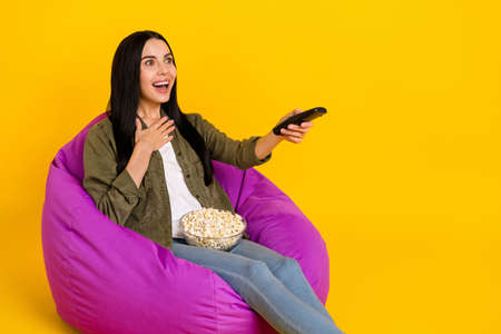 Photo of impressed young lady watch tv wear shirt jeans isolated on yellow backgroundの写真素材
