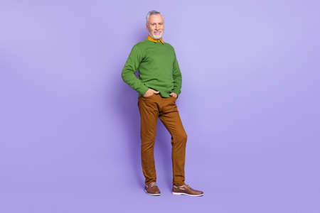 Photo of charismatic retired man wear green sweater walking hands arms pockets isolated violet color backgroundの写真素材