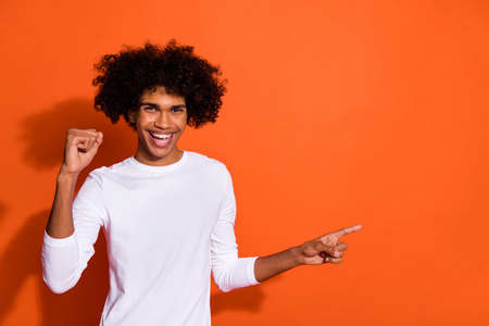 Photo of cool lucky guy dressed white shirt rising finger pointing empty space isolated orange color backgroundの写真素材