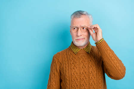 Photo of unsure suspicious retired man wear brown sweater arm spectacles looking empty space isolated blue color backgroundの写真素材