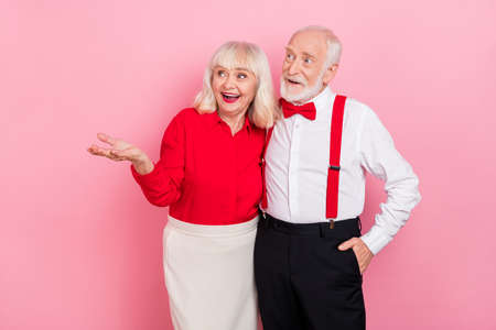 Portrait of attractive cheery amazed gray-haired couple showing copy space isolated over pink pastel color backgroundの写真素材