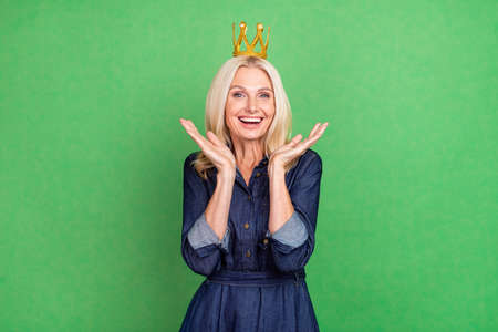Photo of impressed blond old lady wear crown jeans dress isolated on green color backgroundの写真素材