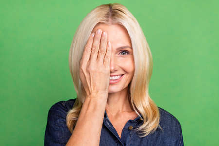 Photo of sweet shy lady pensioner dressed denim outfit hand cover half face isolated green color backgroundの写真素材