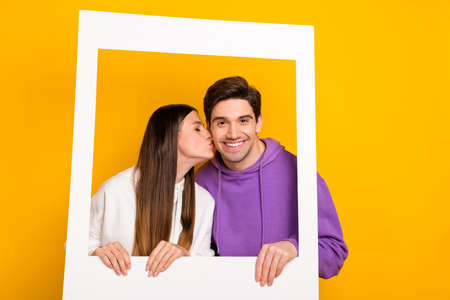 Portrait of two lovely persons picture paper frame kiss cheek isolated on yellow color backgroundの写真素材