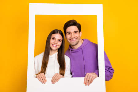 Photo of attractive lady handsome guy hold picture frame beaming toothy smile isolated on yellow...