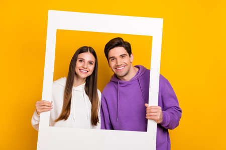 Portrait of two persons hold paper photo frame toothy smile look camera isolated on yellow color backgroundの写真素材