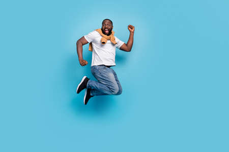 Photo of successful guy jump raise fists have fun wear t-shirt jumper front-tie isolated blue color...