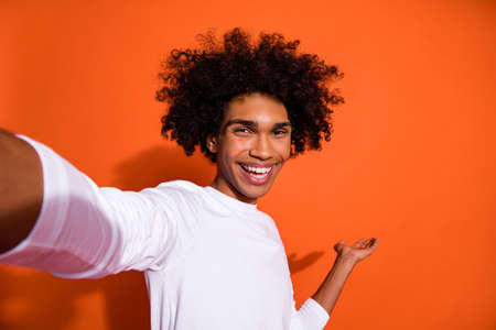 Photo of positive sweet guy wear white shirt recording self video holding arm empty space isolated orange color backgroundの写真素材