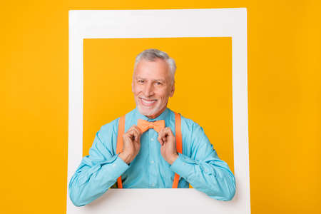 Photo of sweet funny guy pensioner dressed teal shirt hands arms bowtie tacking portrait isolated yellow color backgroundの写真素材