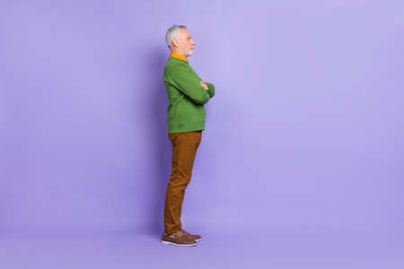 Photo of serious confident man pensioner dressed green pullover arms crossed empty space isolated purple color backgroundの写真素材