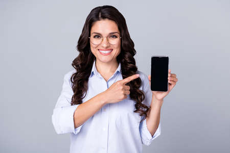 Photo of promoter lady hold phone direct finger side empty space screen wear specs blue shirt isolated grey color backgroundの写真素材