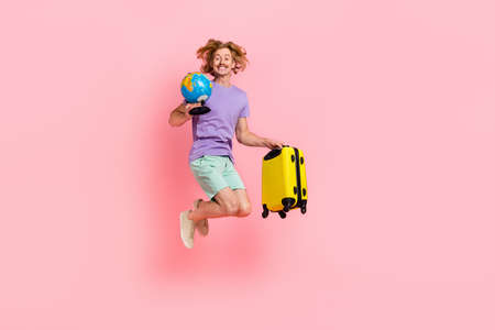 Full length body size view of attractive cheery guy jumping holding bag globe tour resort isolated over pink pastel color backgroundの写真素材