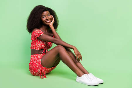 Full length profile photo of sweet millennnial wavy hairdo brunette lady sit wear red outfit footwear isolated on green backgroundの写真素材