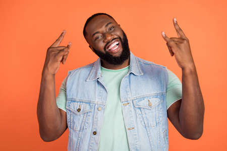 Photo of cool funny afro guy wear denim vest showing hard rock sign isolated orange color backgroundの写真素材