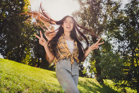 Photo of shiny excited young lady wear checkered shirt glasses smiling walking showing v-signs outdoors urban city parkの写真素材