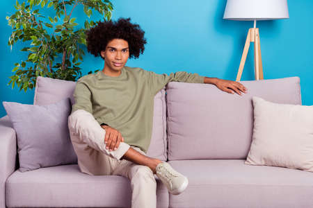 Photo of young handsome man sit divan enjoy free-time wear casual clothes isolated over blue color backgroundの写真素材