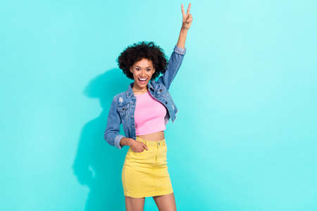 Photo of funny excited young woman wear jeans jacket showing v-sign isolated turquoise color...