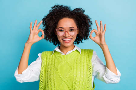 Photo of nice young brunette lady show okey wear eyewear green vest isolated on blue color...