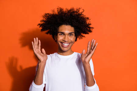 Photo of funny excited guy wear white shirt rising arms smiling isolated orange color backgroundの写真素材