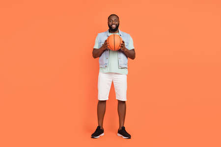 Photo of pretty funky african guy dressed jeans waistcoat playing basketball isolated orange color backgroundの写真素材