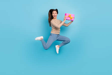 Full length body size view of attractive cheerful funny girl jumping holding giftbox having fun isolated over bright blue color backgroundの写真素材