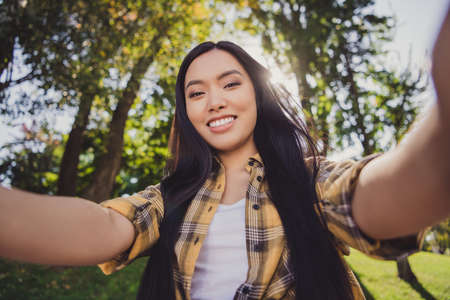 Photo of charming pretty young lady wear checkered shirt smiling walking recording self video outdoors urban city parkの写真素材