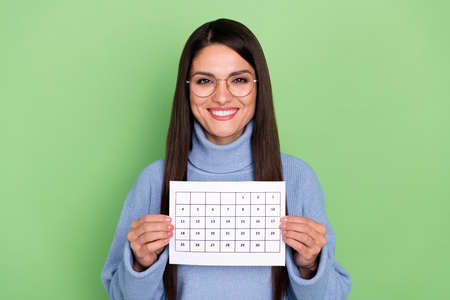 Photo of clever young brunette lady hold calendar wear blue pullover isolated on green color backgroundの写真素材