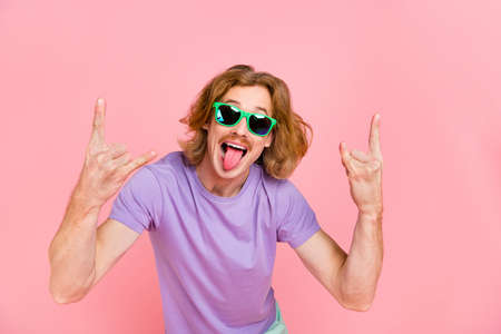 Portrait of attractive cheerful crazy guy showing horn symbol grimacing having fun isolated on pink...