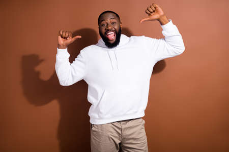 Photo of excited funky guy wear white hoodie smiling pointing thumbs himself isolated brown color backgroundの写真素材