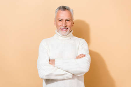 Portrait of attractive content cheerful grey-haired man folded arms isolated over beige pastel color backgroundの写真素材