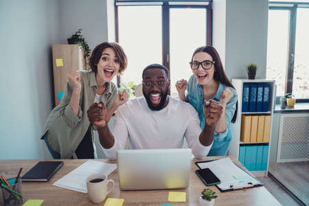Photo of happy excited professionals sitting table winning trades rising fists indoors workplace workstation.の写真素材