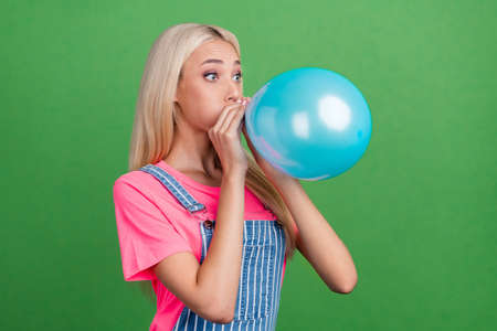 Profile photo of funky crazy lady blow air balloon prepare party wear striped overall isolated green color backgroundの写真素材