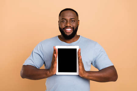 Photo of cool young brunet guy show tablet wear blue outfit isolated on beige color backgroundの写真素材