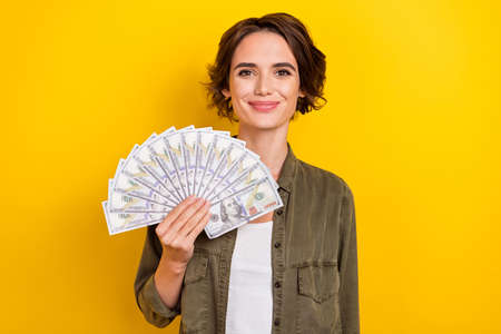 Photo of young pretty woman rich hold banknotes dollars income isolated over yellow color background