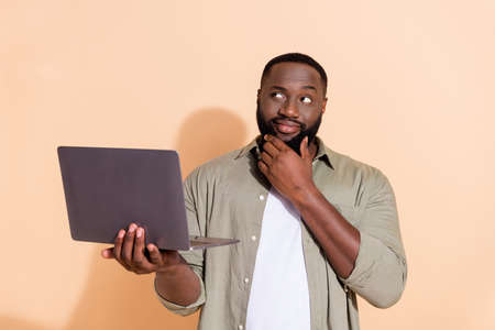 Photo of thinking millennial beard guy hold laptop look up wear grey shirt isolated on beige...