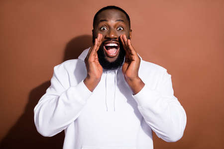 Photo of funny pretty guy wear white hoodie arms lips making announcement isolated brown color...